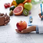 A doctor hold an apple out to a patient across their desk