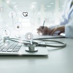 A photo where a laptop and stethoscope sit in the foreground, with a social media network symbol over it. In the backround, a doctor sits writing at a desk.